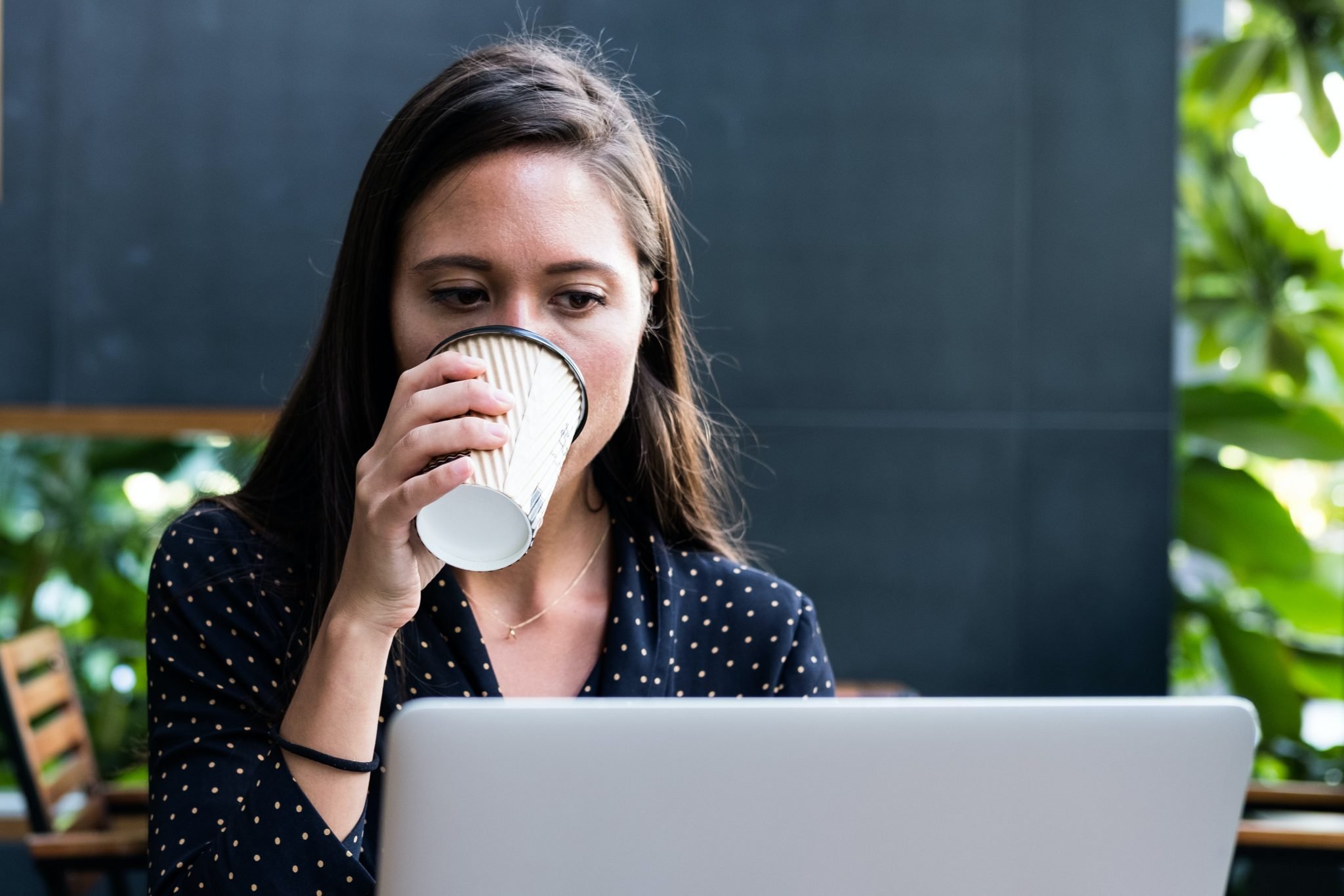 woman facing laptop while holding disposable cup